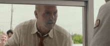 a man in a white shirt and tie is looking through a glass door