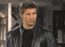 a man wearing a black leather jacket and a black shirt is standing in a room .