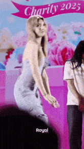 a woman in a blue dress is dancing in front of a banner that says charity 2025