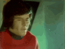 a man in a red shirt looks down with his eyes closed