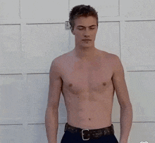 a shirtless man is standing in front of a white wall with his hands folded