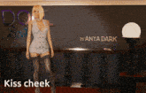 a woman standing in front of a sign that says " kiss cheek "
