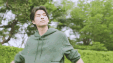 a young man in a green hoodie is standing in front of a tree