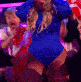 a woman in a blue bodysuit is dancing in a crowd of people .