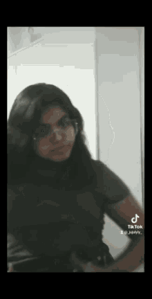 a woman wearing glasses and a black shirt is standing in front of a wall .