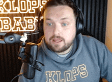 a man wearing headphones stands in front of a microphone with the word klops on his shirt