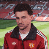 a man wearing a red adidas jacket with a manchester united logo on it