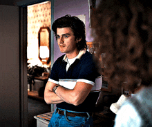 a man in a blue and white striped shirt is standing in a room with his arms crossed