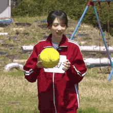 a girl in a red jacket is holding a yellow ball in her hands .