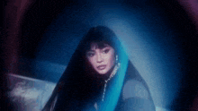 a woman with long hair is wearing a blue scarf around her neck and looking at the camera in a dark room .
