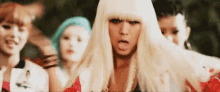a woman in a blonde wig is standing in front of a group of women .