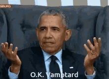 a man in a suit and tie is sitting in a chair and says o.k. vamptard