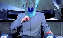 a man in a gray suit is sitting at a desk with a blue helmet on his head .