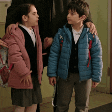 a boy and a girl are standing next to each other and the boy is wearing a blue jacket with the letter x on it
