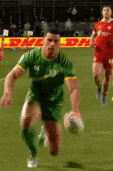 a man is running with a rugby ball on a field with dhl advertisements in the background .