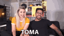 a man and a woman are sitting on a couch with the word toma on the bottom