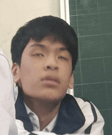 a young man sitting in front of a green chalkboard making a funny face