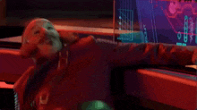 a man in a red jacket is laying on a table in front of a computer screen that says ' ae ' on it
