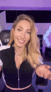 a woman wearing a black and white crop top is smiling and pointing at the camera .