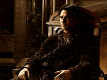 a man with chains around his neck is sitting in a wooden chair