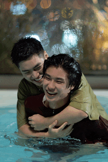 two men are hugging each other in a pool and they are smiling