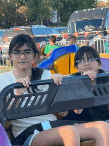 two young girls wearing glasses are riding a roller coaster at a carnival