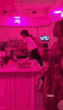 ariana grande is dancing in a kitchen with a pink light on the ceiling .