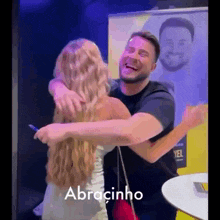 a man and a woman are hugging each other in front of a sign that says abracinho on it .