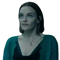 a woman wearing a necklace and a blue sweater looks at the camera