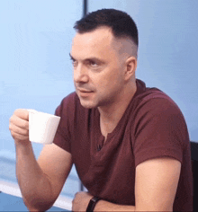 a man in a maroon shirt is holding a white cup of coffee