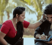 a woman putting her hand on a man 's ear while he writes in a notebook