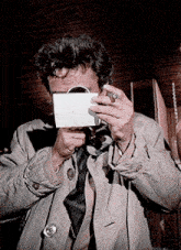 a man in a trench coat and tie is taking a picture with a camera