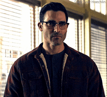a man wearing glasses and a plaid jacket is standing in front of a window with daily tyler hoechlin written above him