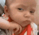 a close up of a baby making a funny face with his hand on his chin .