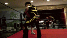 a man in a black and gold outfit is wrestling another man in a red ring