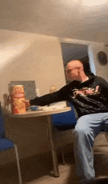 a man is sitting at a table holding a can of chips .