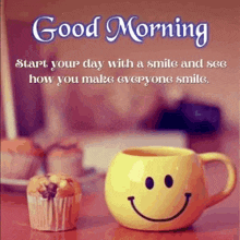 a mug with a smiley face on it is on a table next to a cupcake .