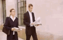 a man and woman are walking down a sidewalk holding newspapers