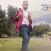 a man in a red jacket is standing in a park giving a thumbs up .