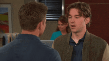 a man in a green jacket talks to another man in front of a nurse