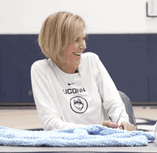 a woman wearing a white uconn shirt is smiling