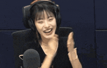 a woman wearing headphones sits in front of a microphone and smiles