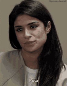 a woman with long dark hair is wearing a tan jacket and a white shirt and is making a funny face .