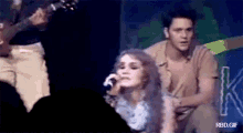 a woman singing into a microphone while a man plays a guitar in the background