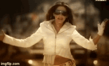 a woman wearing sunglasses and a white jacket is dancing .