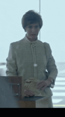 a woman in a suit is standing in front of a window and holding a purse