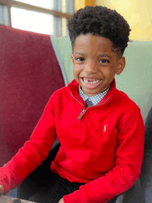 a young boy wearing a red polo sweater smiles for the camera