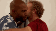 a man in a blue and white shirt is kissing another man in a red shirt