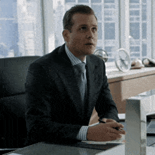 a man in a suit and tie sits at a desk with a pen in his hand
