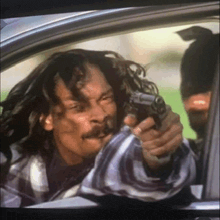 a man with dreadlocks is holding a gun in a car .